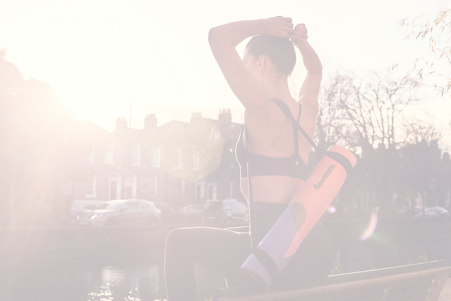 A woman stretching in the sun with a Flowstate yoga mat rolled up on her back