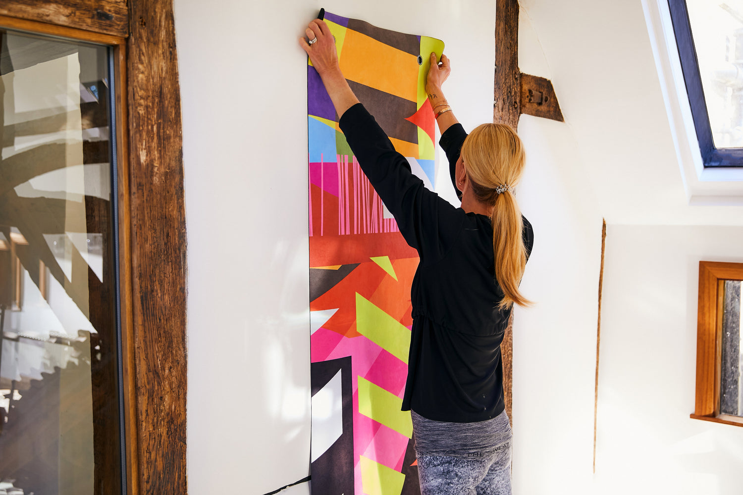 A woman hanging a Flowstate yoga mat on a wall