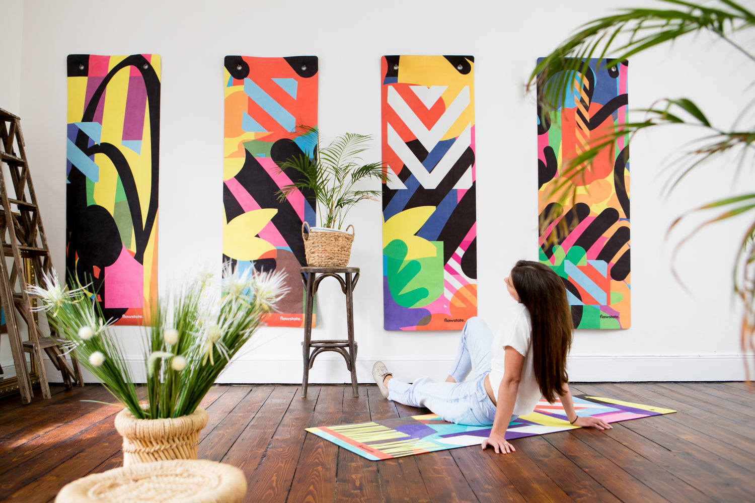 A woman sitting on the floor admiring a wall with four hanging Flowstate yoga mats