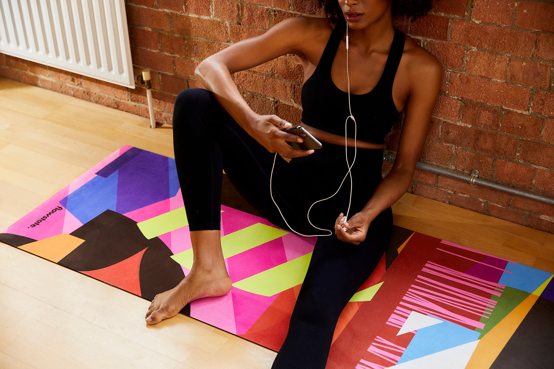 Someone sitting looking at her phone on the Equilibrium 3 Flowstate Yoga Mat 
